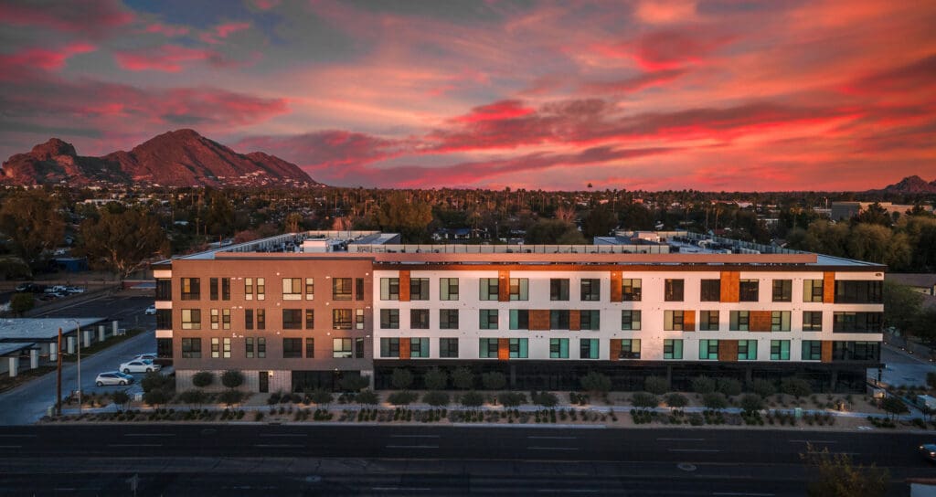Aerial view of a modern office building at sunset with vibrant red skies and distant mountains in the background.