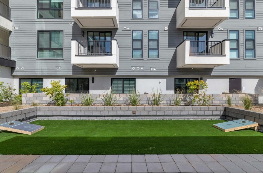 Modern courtyard with artificial grass, cornhole boards, surrounded by a building with balconies and landscaping.