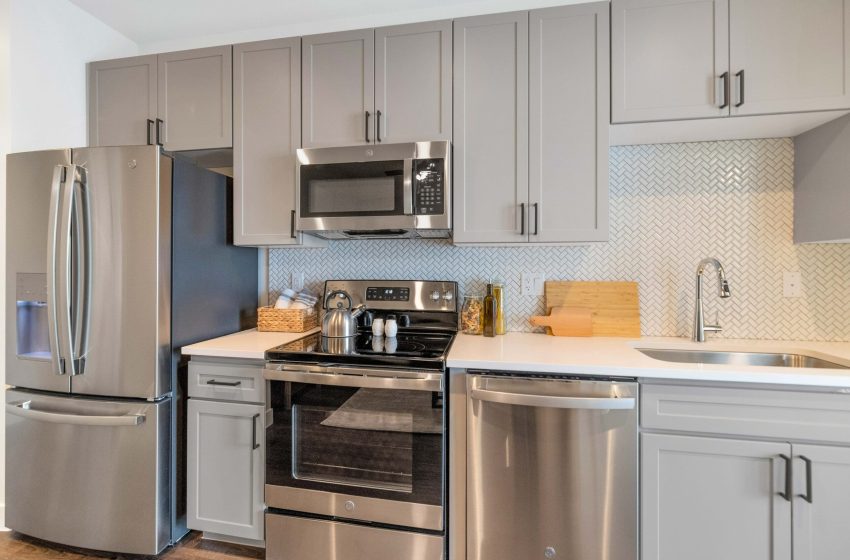 Modern kitchen interior with stainless steel appliances, gray cabinets, and a tiled backsplash.
