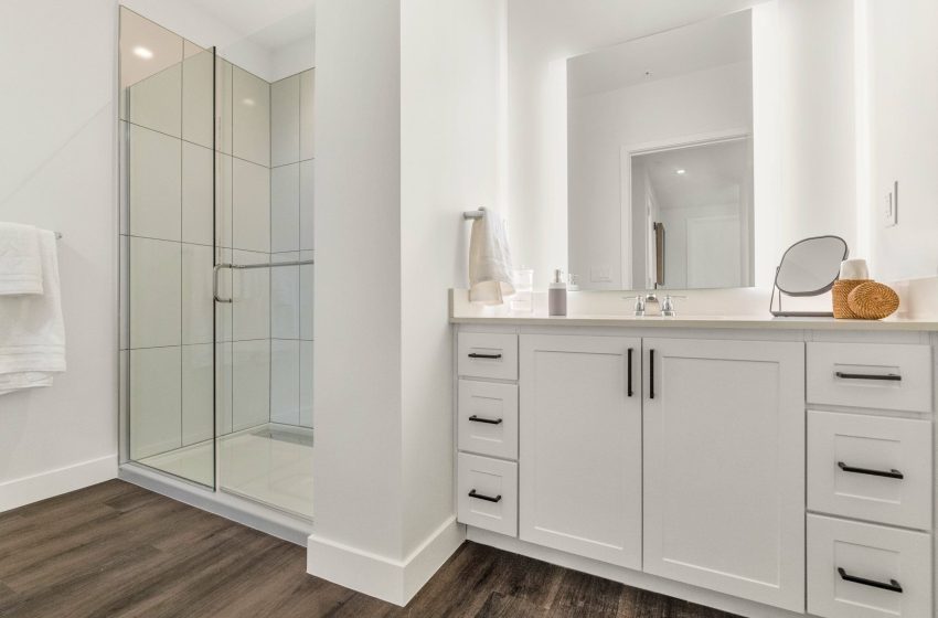 Modern bathroom interior featuring a glass shower stall, white vanity with drawers, and a large mirror above the sink.