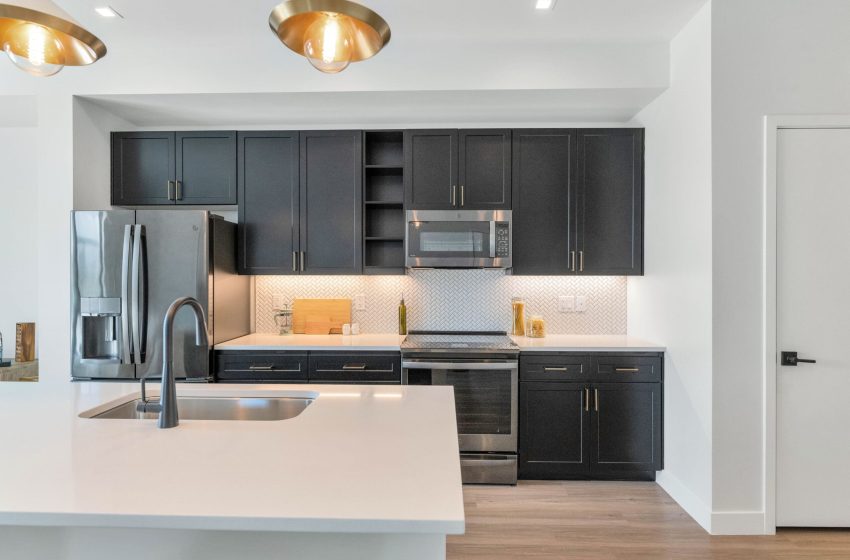 Modern kitchen with dark cabinetry, stainless steel appliances, white countertops, and golden pendant lights.