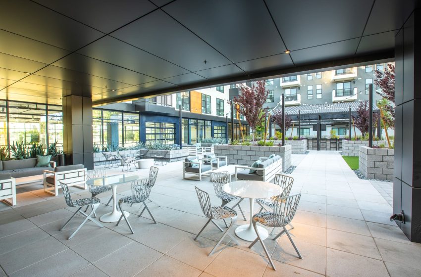 Modern outdoor seating area with stylish metal chairs and tables, set on a paved patio, surrounded by greenery and a contemporary apartment building.