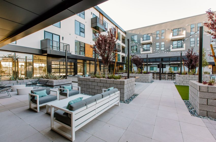 Modern apartment complex with a communal courtyard featuring seating areas, landscaped gardens, and contemporary building architecture.