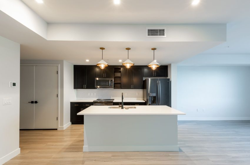 Modern kitchen in an apartment featuring black cabinets, a white island, stainless steel appliances, and pendant lights.