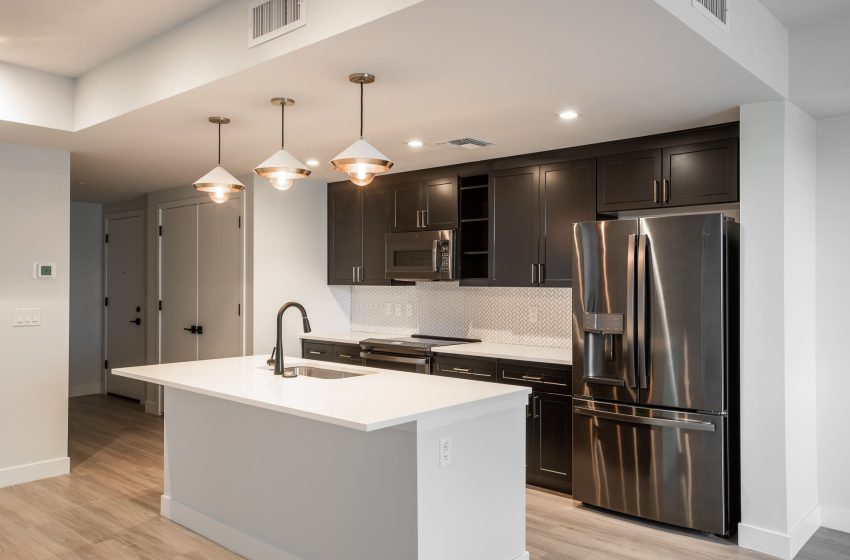 Modern kitchen with dark cabinets, stainless steel appliances, white countertops, and pendant lights.