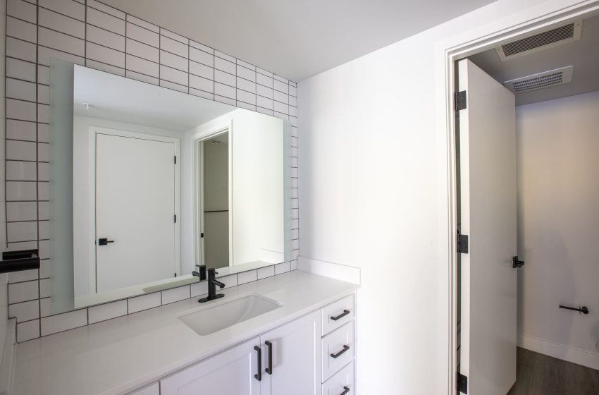 Modern bathroom interior with white subway tiles, a large mirror over a sink with cabinetry, and an open door leading to another room.